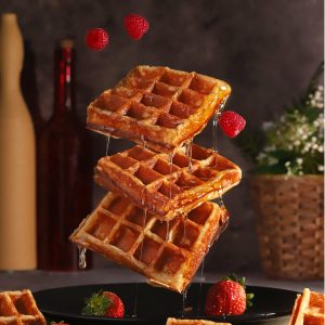 belgische Waffeln mit Obst schwebend vor Flaschen und Pflanze